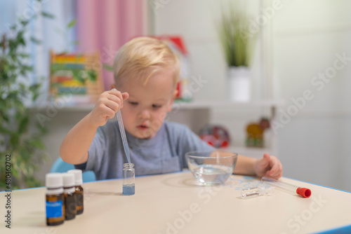 little boy child blonde play chemical experiments to sit at the table at home.