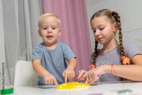 sister and little brother play with yellow slime at table fun at home.