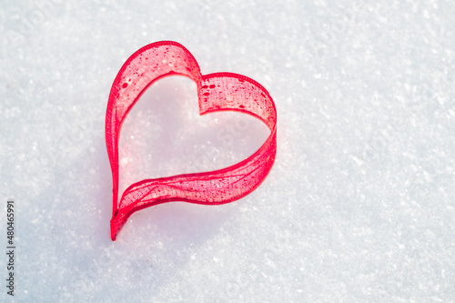 A red heart lies in the snow on a sunny day 