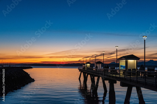 Sun sets over Puget Sound and the Olympic Mountains with colorful skies and a fishing pier