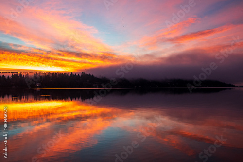 Sunrise over Lake Washington results in a colorful sky and reflection on the water  with foggy forest in the foreground