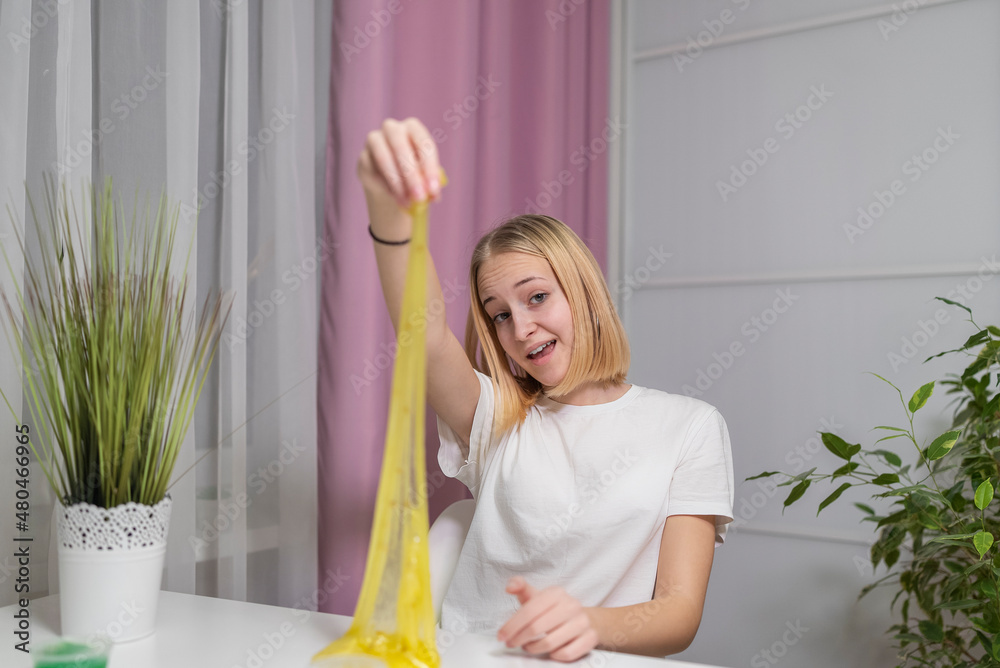 Obraz premium girl playing with yellow shiny slime at the table at home