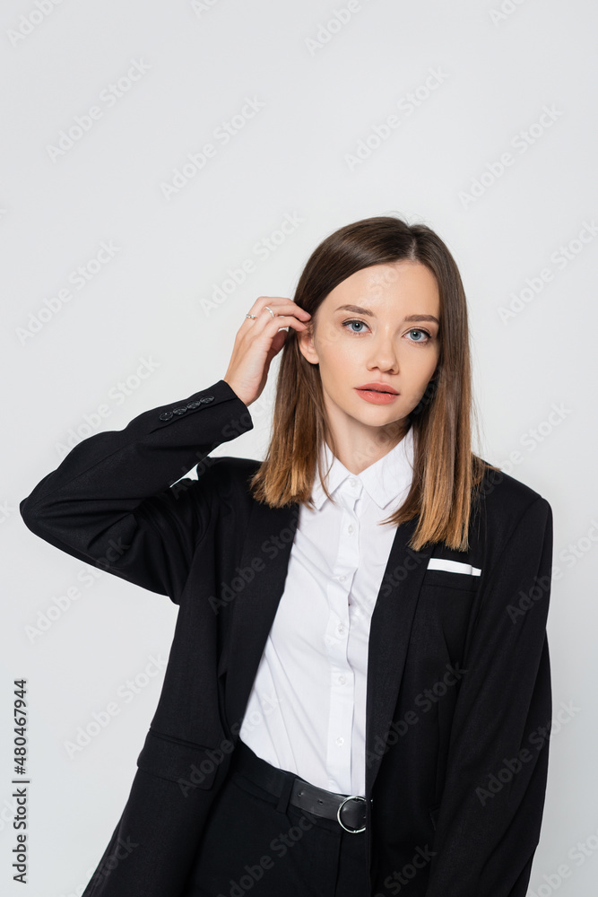 young stylish woman in suit adjusting hair isolated on grey. young stylish woman in suit adjusting hair isolated on grey.