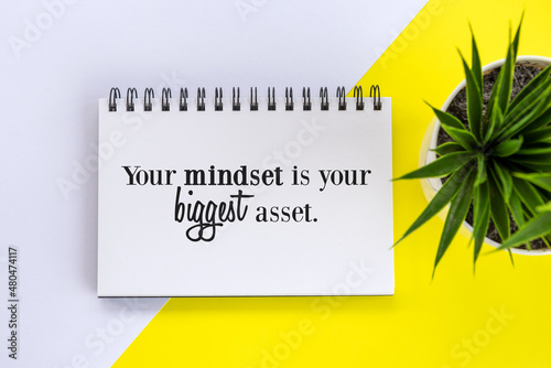 Inspirational motivational quote on a notepaper book - Your mindset is your biggest asset. Business flat lay with plant in a small pot on the white and yellow table background. Positive mind concept. photo