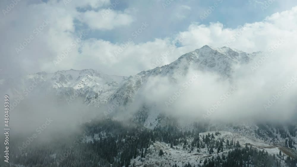 This stock video shows the peaks of snow-capped mountains overgrown with century-old pine trees. White clouds envelop the peaks of the mountains. A road winds through the mountains. This stock video shows the peaks of snow-capped mountains overgrown with century-old pine trees. White clouds envelop the peaks of the mountains. A road winds through the mountains.