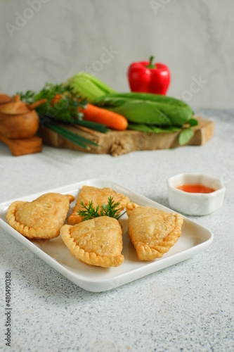 a plate of fried pastries containing vegetables served with sauce against white background 