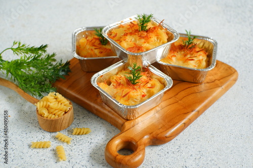 selective focus of  baked macaroni and cheese  in aluminium foil cup against white background 