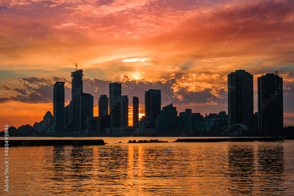 Amazing sunset sky with cityscape in the shadow background. Modern buildings, lake water reflection and