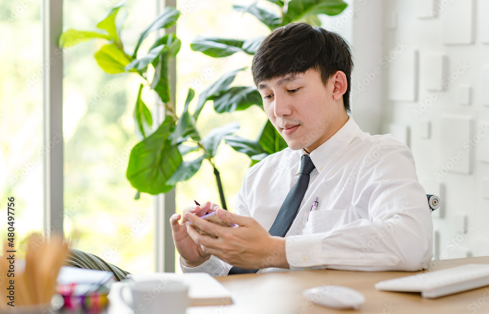 Portrait studio shot of Asian professional successful male businessman employee in formal shirt with necktie sitting look at camera at working desk with computer monitor keyboard mouse and stationery Portrait studio shot of Asian professional successful male businessman employee in formal shirt with necktie sitting look at camera at working desk with computer monitor keyboard mouse and stationery