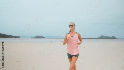 Happy healthy woman runs on the beach with sea on background