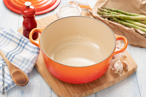 Orange dutch oven on wooden board with ingredients around it