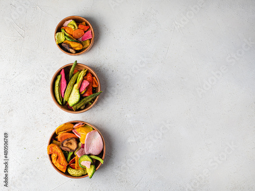 Dehydrated vegan chips in a wooden mango bowl. Vitamin healthy fast food with carrot slices, beetroot wedges, broccoli, zucchini on a light table. food photo banner copy space.