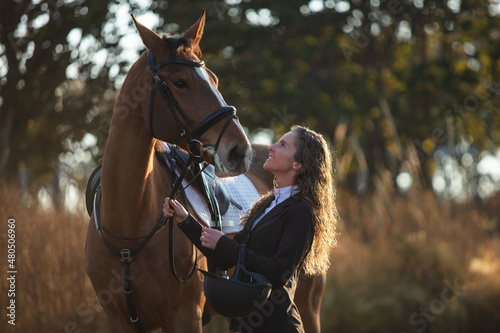 Young woman with curly hair petting her horse in a sunny morning