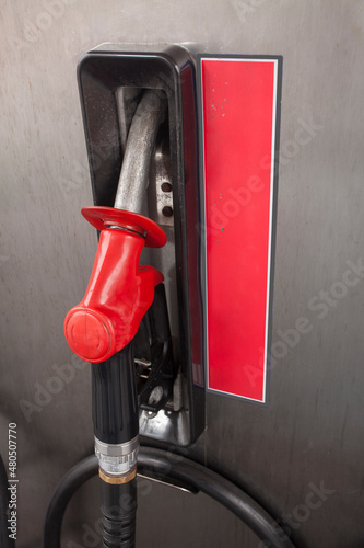 A red fuel nozzle set in the fuel pump, at a petrol station.