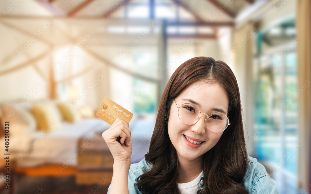 Front view of a pretty Asian woman has a credit card in her hand is booking and checking in for a hotel room with a hotel room background. Online app payment, safety money transferring concept ideas