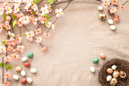 Top view of Easter eggs, nest and flowers on a beige background with copy space. Easter eggs and blooming branches on a textured beige linen background