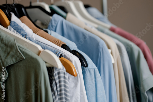 Close-up of a colorful variety of shirts, T-shirts and blouses on hangers inside the closet. boutique of pastel-colored clothing. organic cotton clothing. Selective focus.