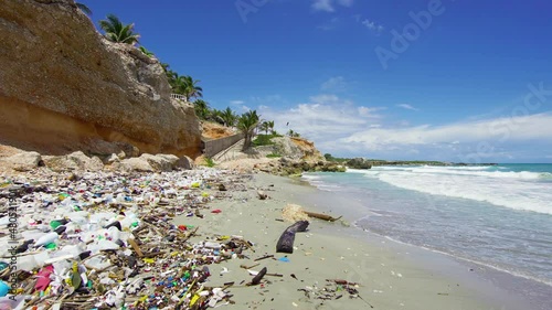 Plastic-littered sandy Dominican beach. Sea waves throw tons of plastic waste ashore every day. The sunny beach is unsuitable for recreation due to pollution with household waste. photo