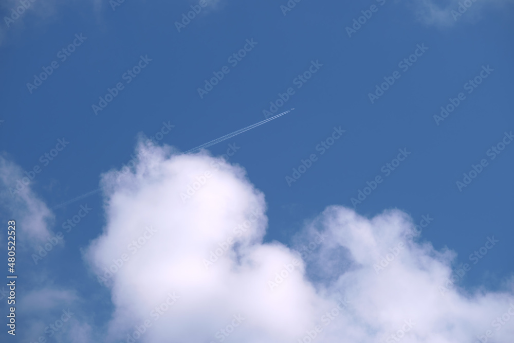 Distant passenger jet plane flying on high altitude on blue sky with white clouds leaving smoke trace of contrail behind. Air traveling concept Distant passenger jet plane flying on high altitude on blue sky with white clouds leaving smoke trace of contrail behind. Air traveling concept