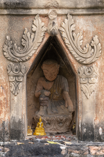 Detail view of shrine with monk sculpture in niche with stucco floral arch decor at ancient Wat Pa Pao Shan buddhist temple, Chiang Mai, Thailand