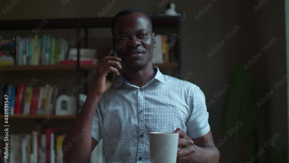Happy African businessman holding cup of coffee talking on the mobile phone in cafe Black people enjoy conversation with friends relax at home