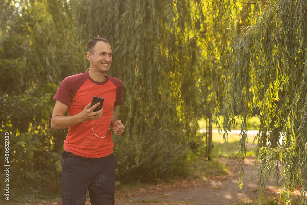 A handsome man in a T-shirt trains in the park and listens to music on headphones A handsome man in a T-shirt trains in the park and listens to music on headphones