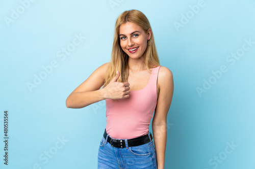 Young Uruguayan blonde woman over isolated blue background giving a thumbs up gesture