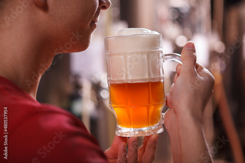 Cropped close up of a professional brewer smiling, smelling freshly brewed beer in a mug