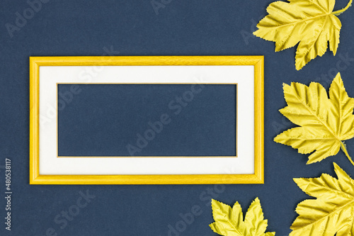 Creative layout, delicate yellow frame with a white passe partout with an empty space for the slogan, Golden leaves, Flat lay, Abstract colors, dark, navy blue background photo