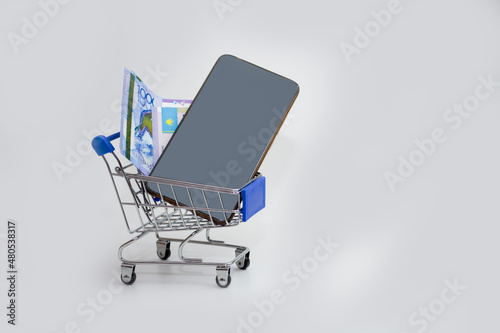 In the trolley on a white background is a phone with a tenge bill, buying a phone, or paying through mobile applications. photo
