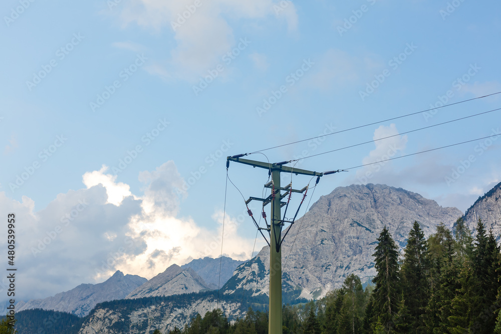 Electric poles near the mountain have green trees.