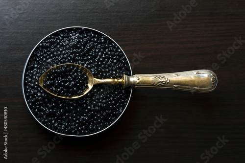 LUXURY GOLDEN SPOON IN BELUGA CAVIAR TIN CAN ON DARK WOODEN BACKGROUND. TOP VIEW. photo
