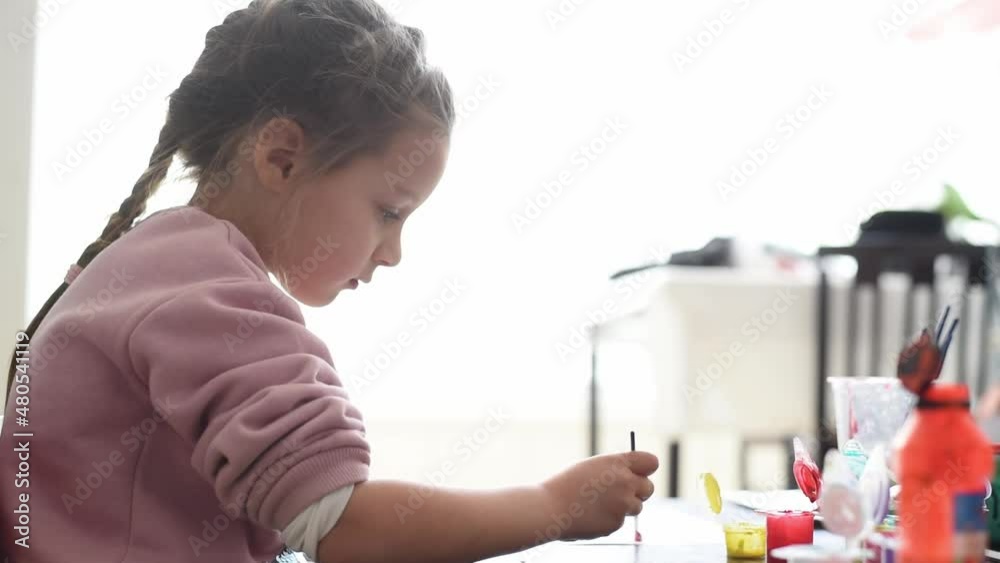 Small, beautiful girl in pink sweater draws of paints. Child very likes drawing. Development of fine motor skills important in childhood. Creativity for children at home. Small, beautiful girl in pink sweater draws of paints. Child very likes drawing. Development of fine motor skills important in childhood. Creativity for children at home.