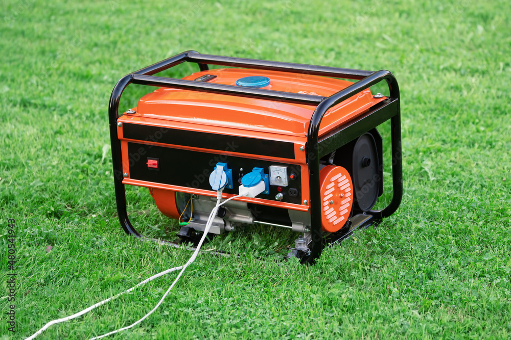 Portable electric generator with electric wires connected on the green grass in summer - obrazy, fototapety, plakaty 