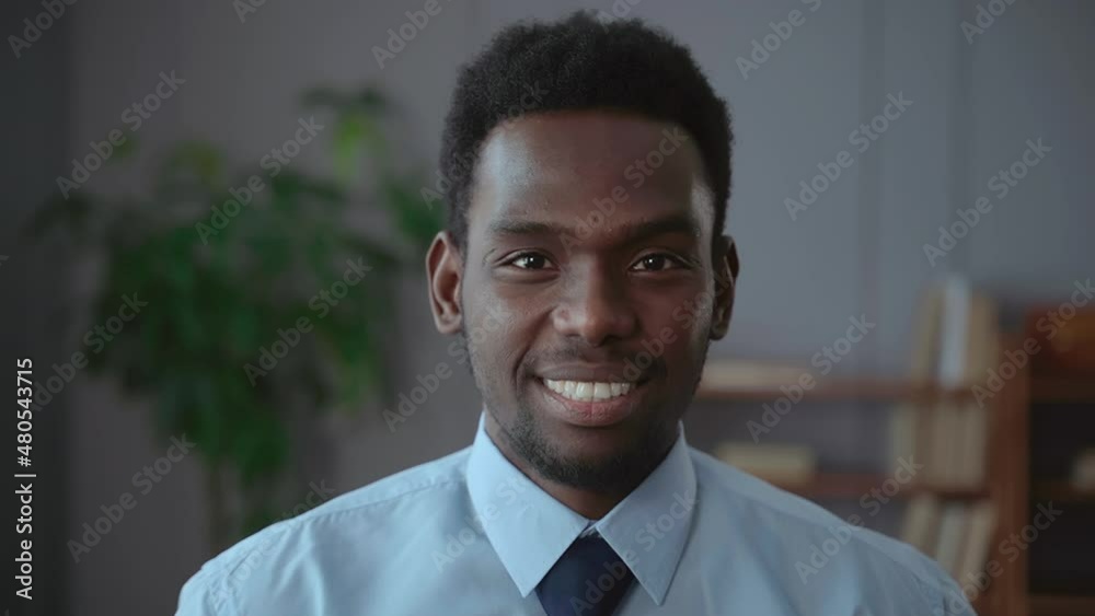 Portrait of young businessman posing and smiling for camera while standing in business office spbas. Closeup view of african bearded man looks with toothy smile and poses, has work break and stands in Portrait of young businessman posing and smiling for camera while standing in business office spbas. Closeup view of african bearded man looks with toothy smile and poses, has work break and stands in