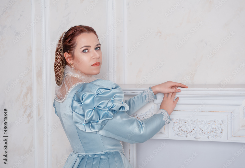 Beautiful young woman in medieval style blue dress stand near fireplace Beautiful young woman in medieval style blue dress stand near fireplace