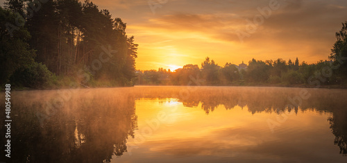 Fototapeta Naklejka Na Ścianę i Meble -  Orange summer sunrise over the forest lake with mist and sun reflected in the water
