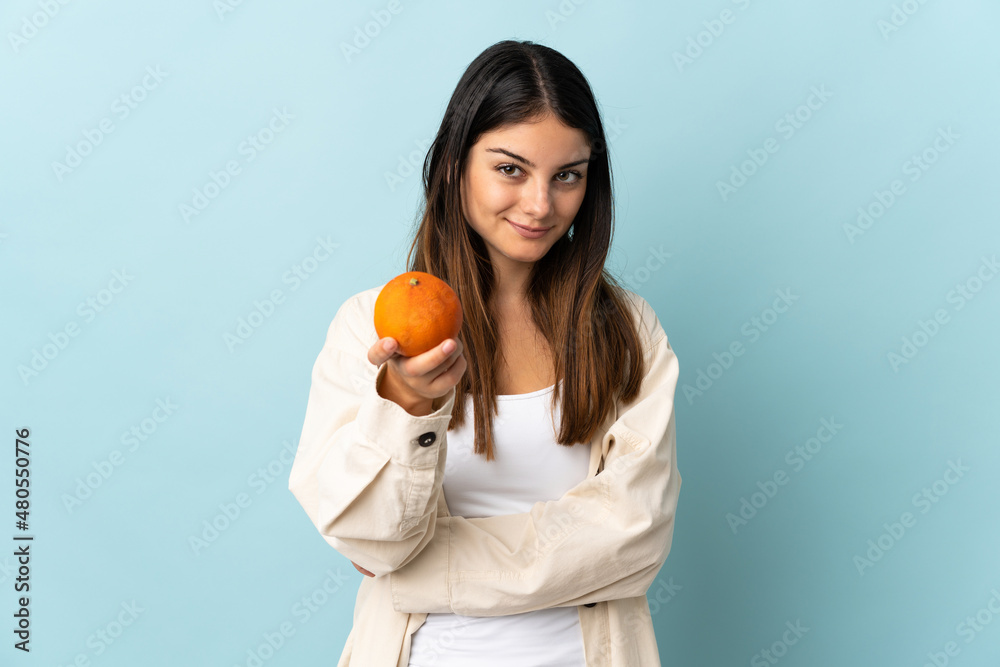 Young caucasian woman isolated on blue background holding an orange Young caucasian woman isolated on blue background holding an orange