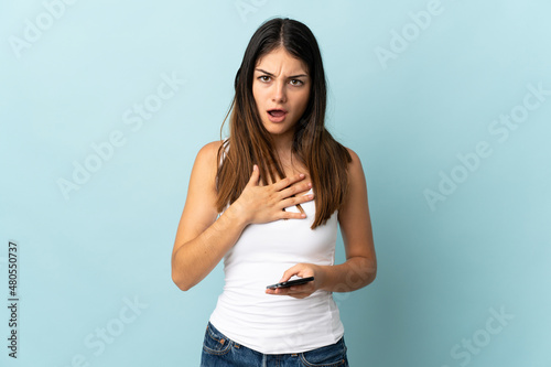 Young caucasian woman using mobile phone isolated on blue background surprised and shocked while looking right © luismolinero