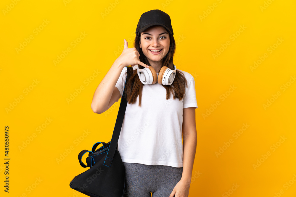 Young sport woman with sport bag isolated on yellow background making phone gesture. Call me back sign Young sport woman with sport bag isolated on yellow background making phone gesture. Call me back sign