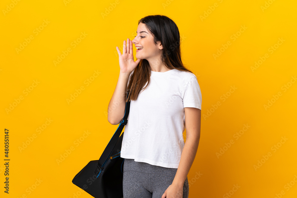 Young sport woman with sport bag isolated on yellow background shouting with mouth wide open to the side Young sport woman with sport bag isolated on yellow background shouting with mouth wide open to the side