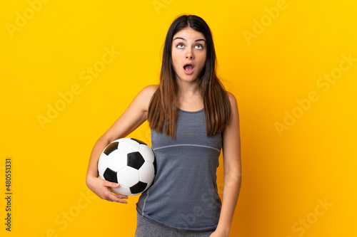 Young football player woman isolated on yellow background looking up and with surprised expression © luismolinero