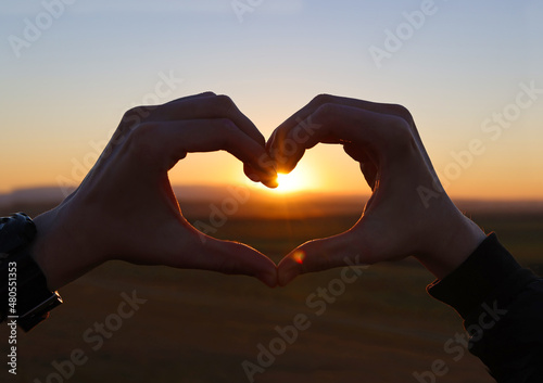 Hands of a teenage boy in the form of heart with the sunlight passing through the hands in sunset sky, twilight time. Hands in shape of love heart. Love concept