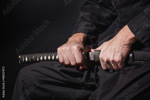 The samurai holding a Japanese katana sword. Photo of a warrior dressed in black clothes in low key with selective focus
