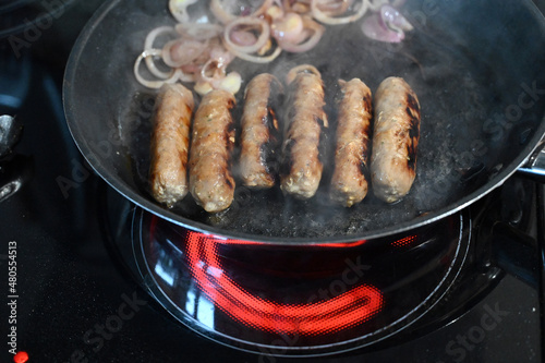 sausages and sliced red onion cooking in a frying pan
