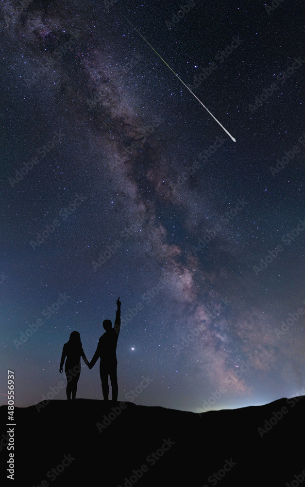 Fototapeta premium A couple of people in love hold hands and look at a shooting star at night against the backdrop of the Milky Way. The silhouettes are drawn by hand without a reference image. 