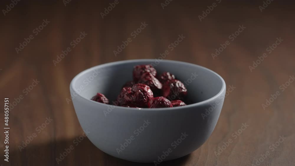 Slow motion freeze-dried cranberries taken by man hand from blue bowl on wood table with copy space Slow motion freeze-dried cranberries taken by man hand from blue bowl on wood table with copy space