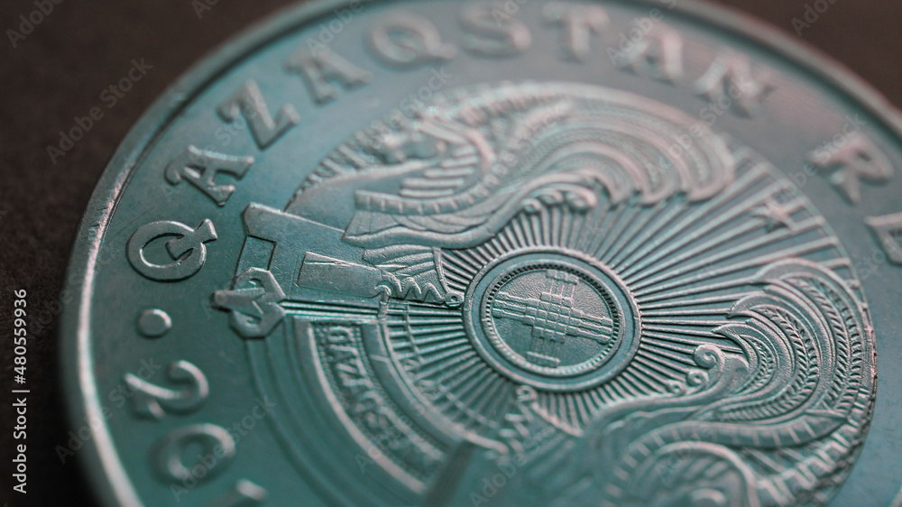 Translation: Kazakhstan. Kazakh 50 tenge coin with the country emblem and focus on shanyrak. Close-up. Green tinted background or wallpaper for Kazakh economy or state. Macro