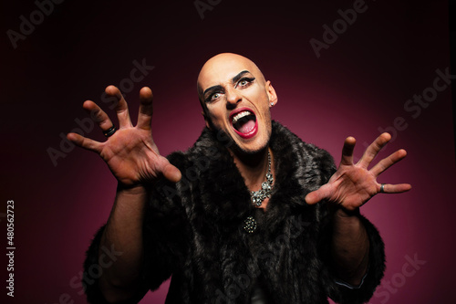 Scary freaky screaming gender fluid transgender gay man with shaved head wearing fancy makeup and fake fur coat, Halloween or horror story style