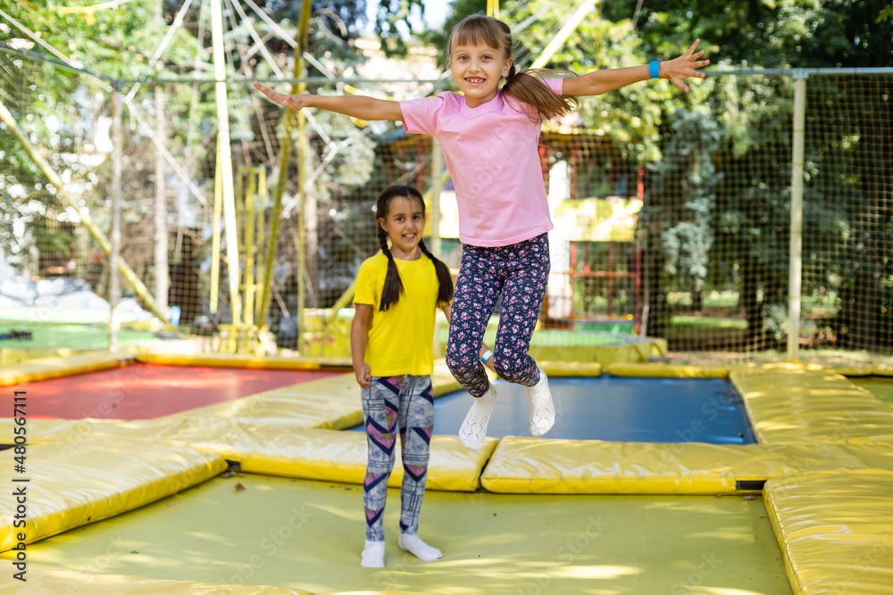 Two little girls in the summer jump on a trampoline, smiling and ...